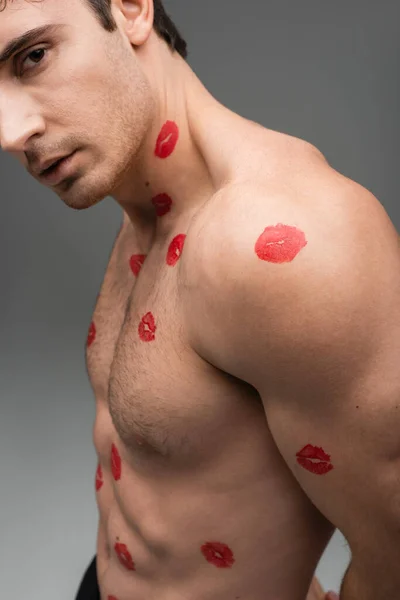 Cropped view of shirtless muscular man with red kiss prints on body isolated on grey - foto de stock
