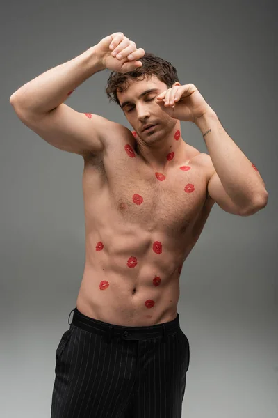 Sexy shirtless man with red lipstick marks on body posing with closed eyes on grey background — Stock Photo