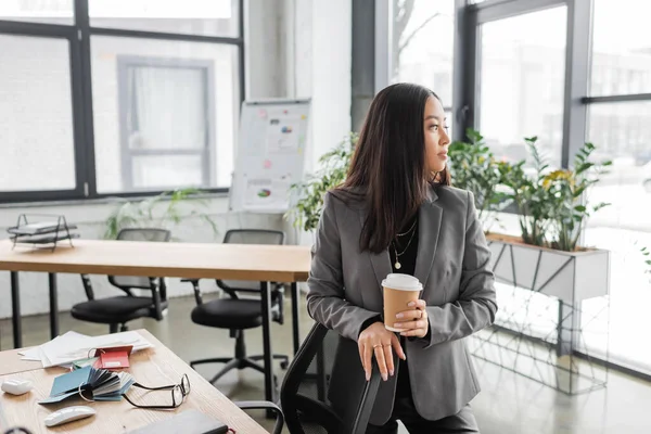 Young asian interior designer holding coffee to go near working table in office - foto de stock