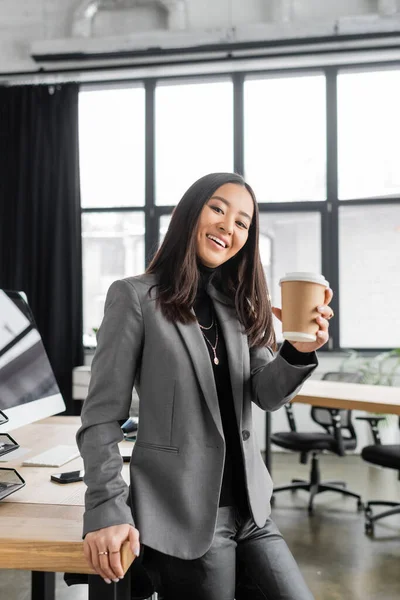Smiling asian interior designer holding coffee to go in office - foto de stock