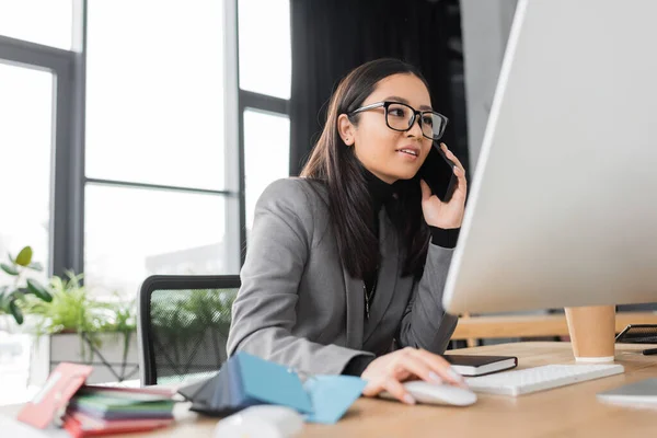 Young asian designer talking on mobile phone and using computer in office — Stock Photo