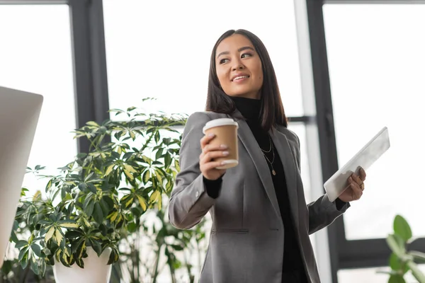 Cheerful asian interior designer holding coffee to go and digital tablet in office — Foto stock