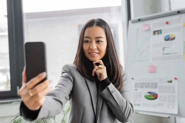 Brunette asian interior designer using blurred smartphone in office — Stockfoto