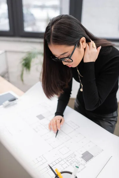 Asian interior designer in eyeglasses working with blueprint in office — Photo de stock