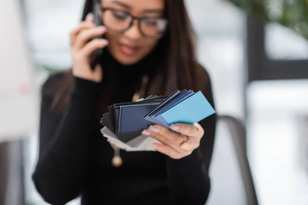 Blurred designer talking on smartphone and holding color samples in studio — Stock Photo