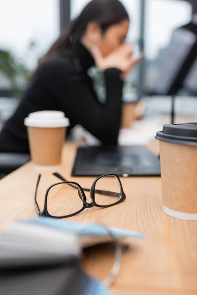 Eyeglasses and coffee to go near blurred designer in studio — Stock Photo