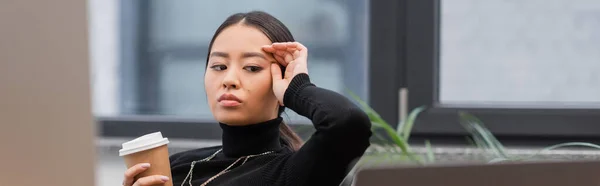 Asian designer suffering from headache and holding coffee near computers in office, banner — Photo de stock