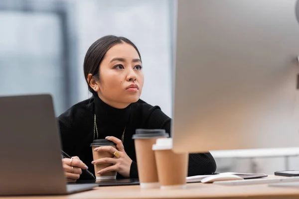 Молодой азиатский дизайнер интерьера работает с компьютерами возле кофе, чтобы пойти в офис — стоковое фото