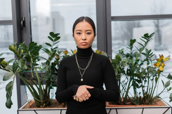 Portrait of asian interior designer looking at camera near plants in office — Stock Photo