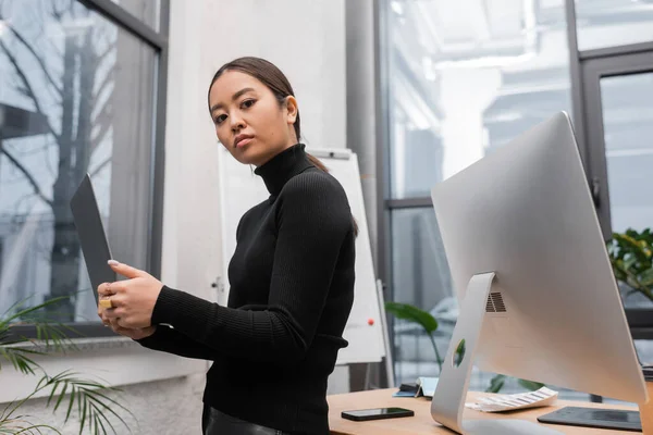 Young asian interior designer holding laptop near devices in office — Photo de stock