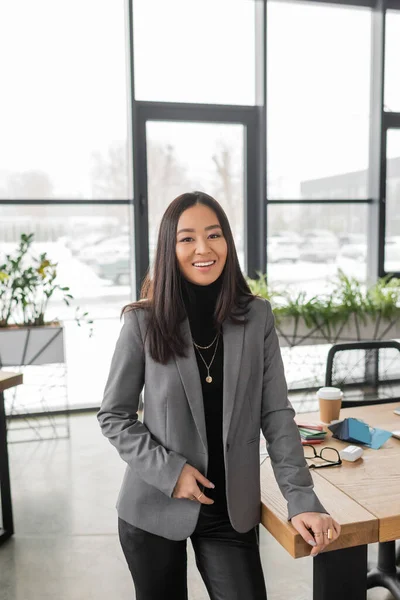 Positive asian designer looking at camera near working table in design studio — Stock Photo