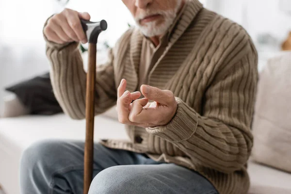 Cropped view of senior man with parkinson disease holding walking cane while sitting on couch at home — Foto stock