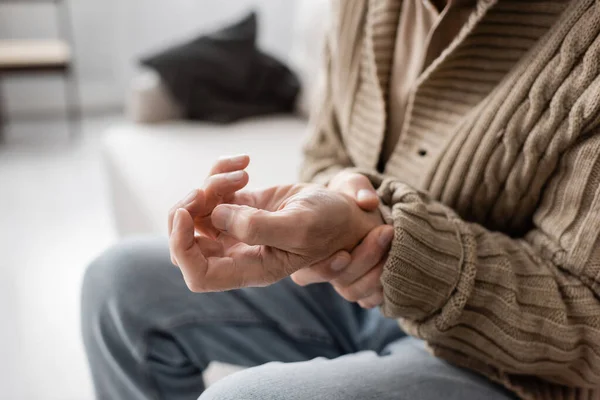 Partial view of senior man with parkinsonism holding trembling hand while sitting at home — Foto stock