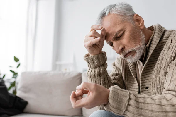 Grey haired man with parkinson syndrome and tremor in hands sitting with closed eyes on couch at home — Stock Photo