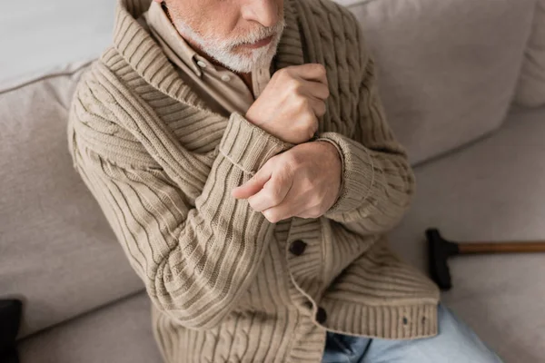 Cropped view of senior man in knitted cardigan suffering from parkinsonism and tremor in hands while sitting at home - foto de stock