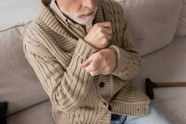 Cropped view of senior man in knitted cardigan suffering from parkinsonism and tremor in hands while sitting at home — Stock Photo