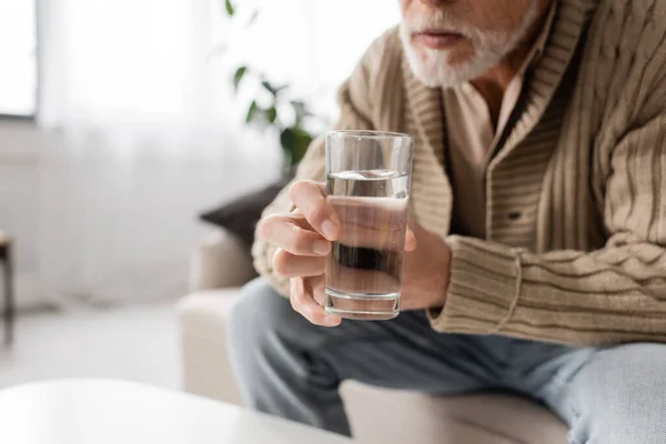 Partial view of senior man with parkinson disease holding glass of water in trembling hands — Foto stock