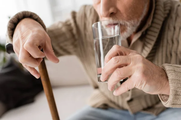 Частковий вид на старшого чоловіка з паркінсонізмом і тремор в руках питна вода вдома — стокове фото