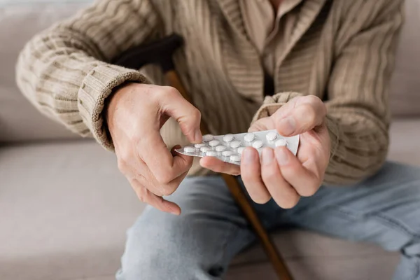 Partial view of aged man suffering from parkinsonism and holding pills in trembling hands while sitting at home — Stock Photo