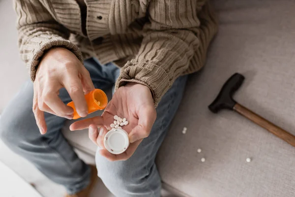 Cropped view of aged man suffering from parkinsonism and holding container with pills while sitting on couch — Stockfoto