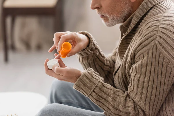 Боковой вид больного болезнью Паркинсона, держащего в руках контейнер с таблетками — стоковое фото