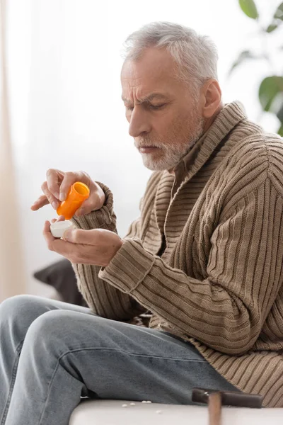 Senior man in knitted cardigan holding pills container in trembling hands while suffering from parkinson disease — Stock Photo