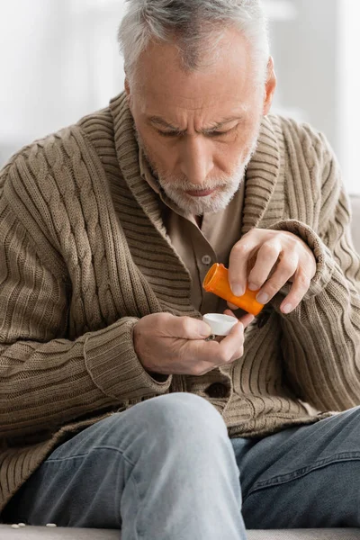 Grey haired man in knitted cardigan holding pills from parkinson disease in trembling hands — Stock Photo