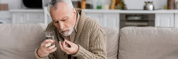 Senior man holding pill and glass of water in trembling hands while suffering from parkinson syndrome, banner — Foto stock