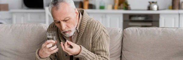 Senior man holding pill and glass of water in trembling hands while suffering from parkinson syndrome, banner — Stock Photo