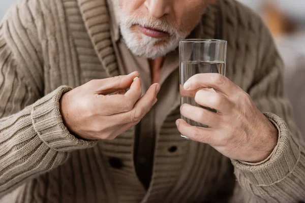 Partial view of senior man with parkinson disease holding pill and glass of water in trembling hands — Stock Photo