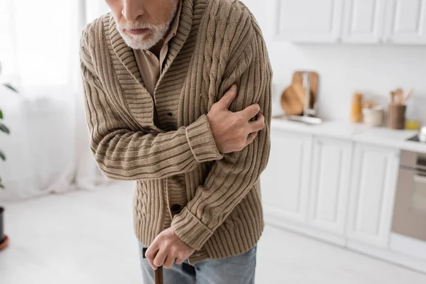 Cropped view of aged man with parkinson disease standing in knitted cardigan with walking cane in kitchen — Fotografia de Stock