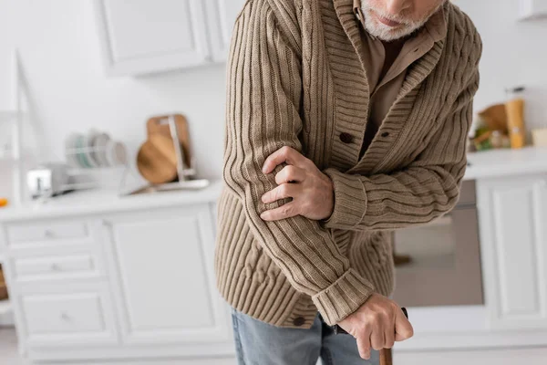 Partial view of senior man with parkinson disease and hands tremor standing with walking cane in kitchen — Stock Photo