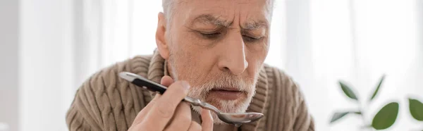 Старший бородатый мужчина страдает от паркинсонизма и держит ложку во время ужина на кухне, баннер — стоковое фото