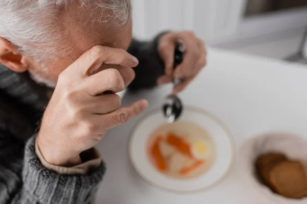 High angle view of man with parkinson syndrome and trembling hands holding spoon near blurred soup in kitchen — Stock Photo