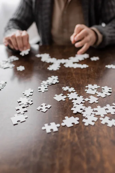 Selective focus of jigsaw puzzle elements near cropped man with parkinson syndrome on blurred background - foto de stock
