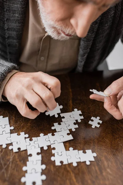 Обрезанный вид пожилого человека с болезнью Паркинсона и дрожь в руках, комбинирующих головоломку на столе дома — стоковое фото