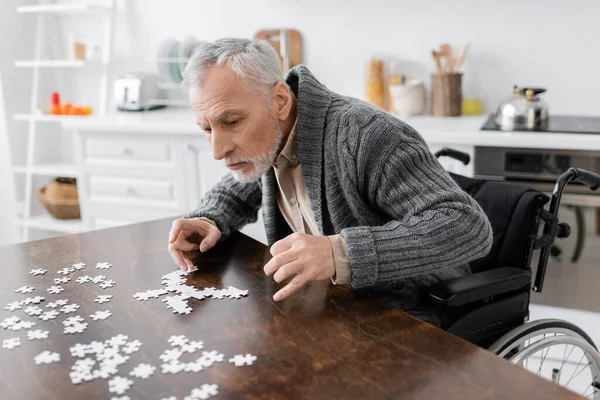 Человек с инвалидностью и синдромом Паркинсона сидит рядом с головоломкой на столе дома — стоковое фото