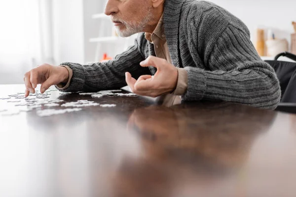 Обрезанный вид человека с болезнью Паркинсона и дрожащие руки, сидящие возле головоломки дома — стоковое фото