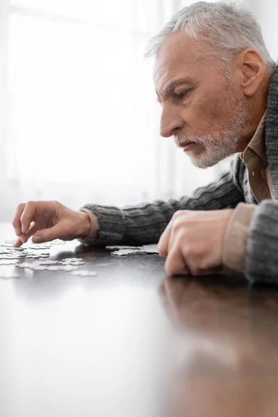 Side view of aged man with parkinson syndrome combining jigsaw puzzle at home — Stock Photo