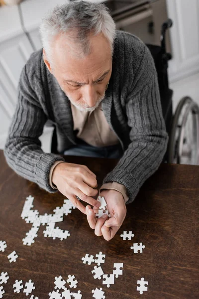 High angle view of man with parkinsonian syndrome sitting in wheelchair and holding elements of jigsaw puzzle in trembling hands — Stock Photo