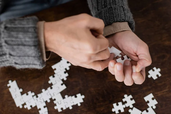 Cropped view of senior man suffering from parkinsonism and holding elements of jigsaw puzzle in trembling hands — Stock Photo