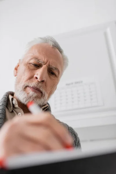 Низкий угол зрения бородатый пожилой человек с болезнью Альцгеймера записи в размытой тетради дома — стоковое фото
