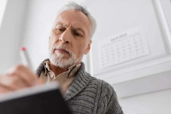 Low angle view of grey haired man with alzheimer syndrome writing in blurred notebook — Stock Photo