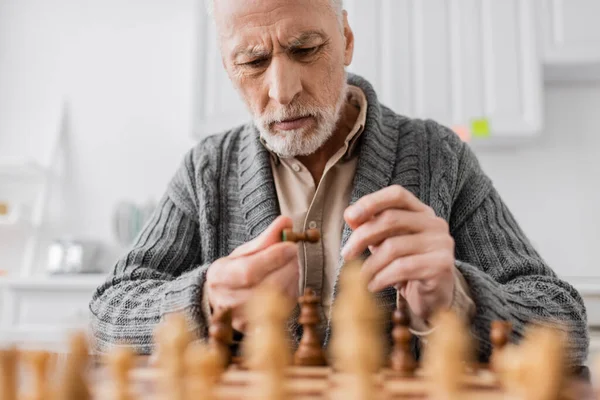 Tensed man with alzheimer syndrome looking at chess figure near chessboard on blurred foreground — Photo de stock