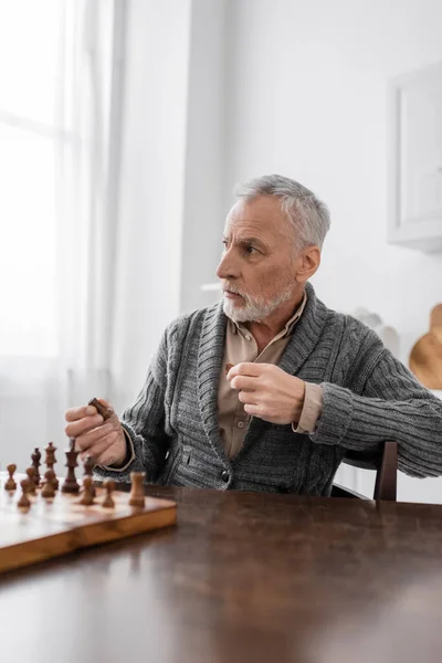 Aged man with alzheimer disease holding chess figure and looking away - foto de stock