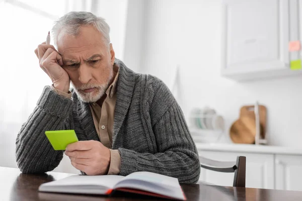 Thoughtful man suffering from memory loss and looking at sticky notes near blurred notebook — Photo de stock