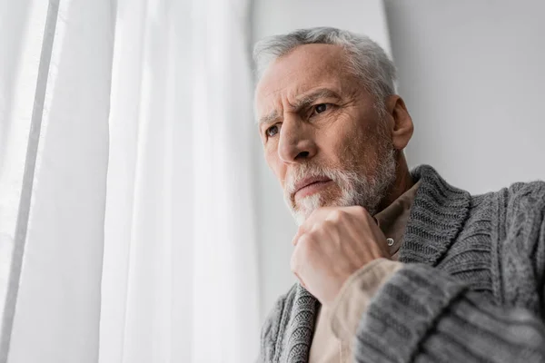 Tense man suffering from memory loss caused by alzheimer disease standing with hand near chin at home — Stockfoto