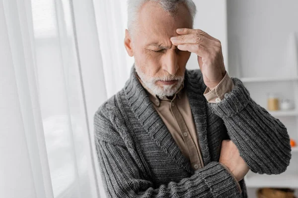 Depressed senior man with alzheimer syndrome standing with closed eyes and touching forehead at home — Stock Photo