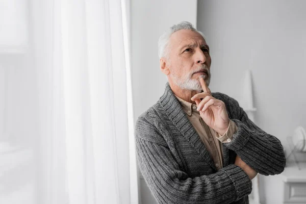 Grey haired man holding hand near chin and looking away while suffering from memory loss caused by alzheimer syndrome — Stock Photo