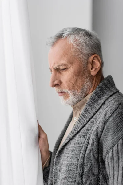 Side view of depressed senior man with alzheimer diseased looking away near window at home - foto de stock